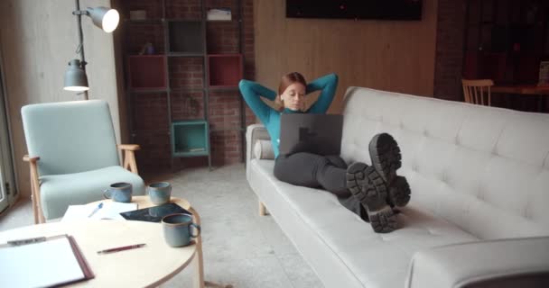 若い女性はソファの上で休んで 彼女のラップトップで働いていますカフェテリア オレンジ トラック運動 — ストック動画