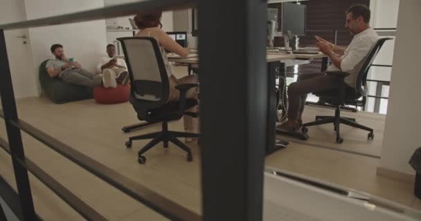 オフィスの労働者のカメラの傾きの動き いくつかは働いていて 他の人は勤務時間 多様な民族性と人種の間に居心地の良いソファーで休んでいる — ストック動画