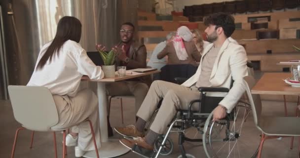 坐在轮椅上的商人来到办公室 与他的同事们在办公室咖啡店区 卡车运动区进行讨论 — 图库视频影像