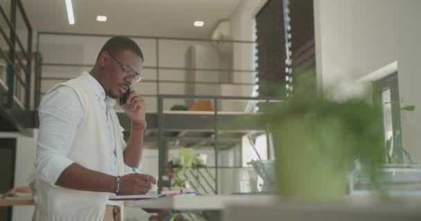 デスクで一人で働く黒人男性は 同僚がバックグラウンドで作業している間 夏時間のオフィス労働条件 — ストック動画