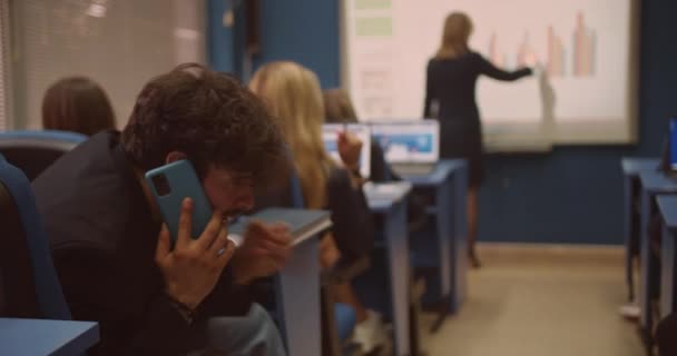 授業中に電話会話をする生徒の1人が スマートボードにノートを書き 大学の授業で生徒に講義をする — ストック動画