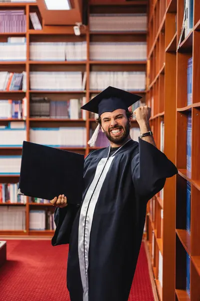 Young Excited Graduate Wearing Cap Gown While Holding His Bachelor — Stock Photo, Image