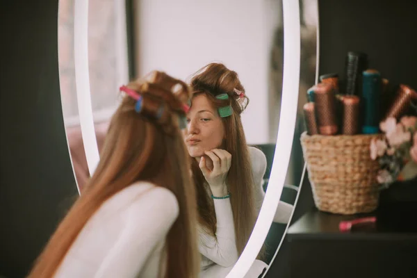 Beautiful ginger girl looking at the mirror while sitting at the hair salon