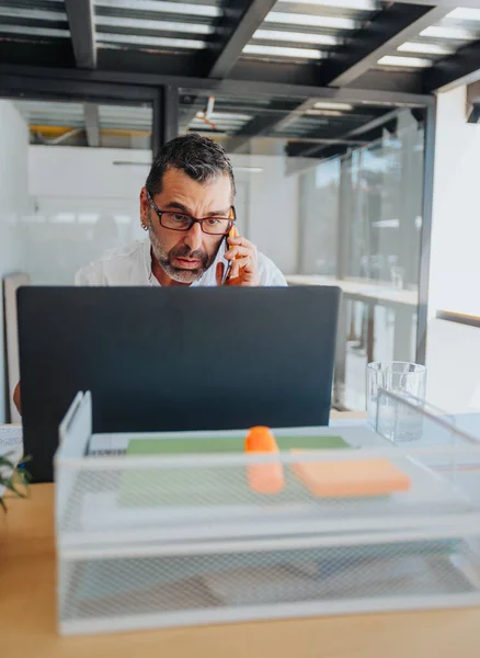 Üst Düzey Olgun Adamının Ofiste Dizüstü Bilgisayarla Çalışırken Telefonla Konuşması — Stok fotoğraf