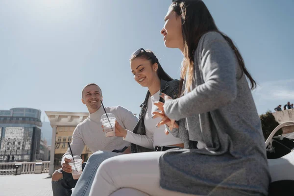 Close up of group of three friends smiling and sitting at the center of the city and drinking milkshakes