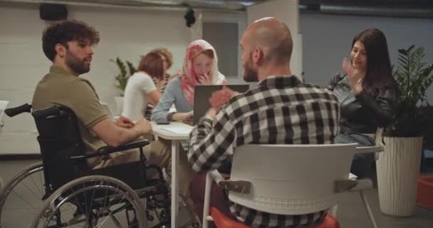ビジネスセミナーに参加する多様な人々のためのオフィスでの独占的な環境 車椅子の1人の男性同僚が積極的に協力 — ストック動画