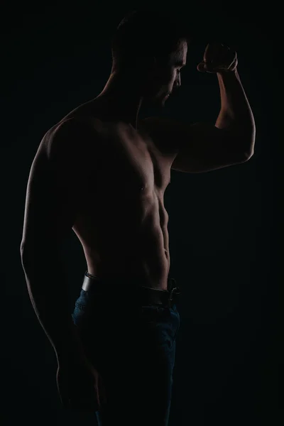 Stunning and well-built man standing in front of a dark background and flexing his muscles
