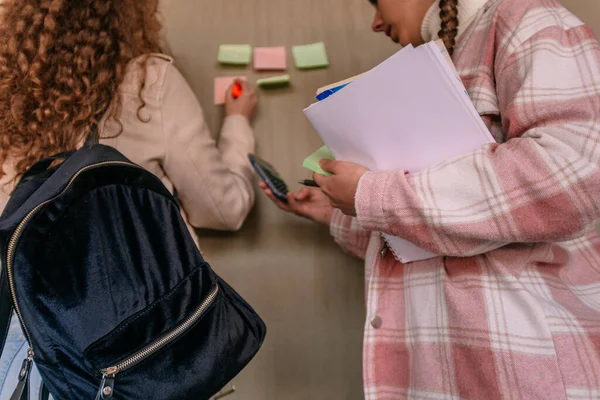 彼女の友人が壁に粘着性のノートに結果を書いている間 電卓を使用する学校の少女 — ストック写真