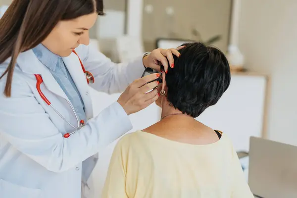 老年妇女在现代医务室接受耳镜检查 熟练和经验丰富的医生检查她年老的病人的耳朵 — 图库照片