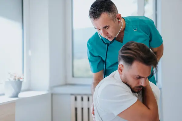 高齢の医師は 設備の整った診療所で若い男性患者に医療を提供し 血圧をチェックし 健康問題を議論する — ストック写真