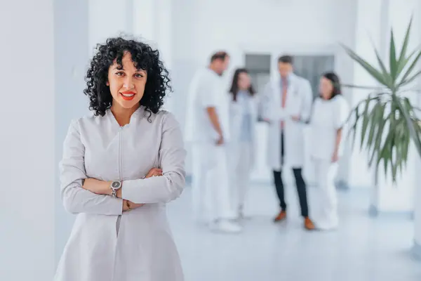 一名身穿白色实验室外套的有信心的女医生 双手交叉地摆出姿势 她带着满意的微笑 流露出专业精神和成功 — 图库照片