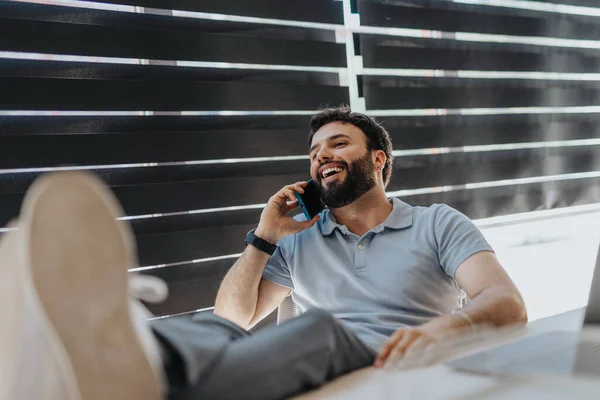 Satisfied businessman smiling during phone call while sitting at the office with his feet on the desk.