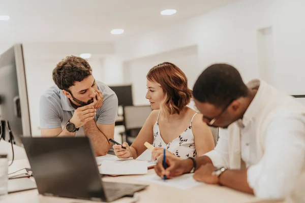 A team of business employees collaborates in a office, discussing profit statistics and strategizing together. They work on projects, fostering positive working atmosphere and effective communication.