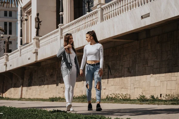 建物の前に公園で手を握りながら歩いている2人の美しいブルネットの少女 — ストック写真