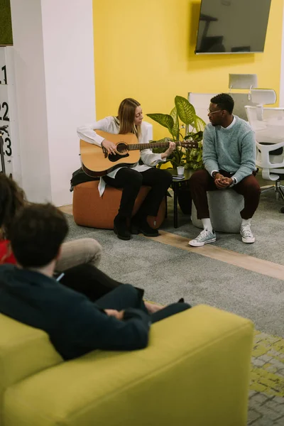 Multiracial coworkers having karaoke at the office after hard day at work. Lovely blonde businesswoman playing guitar and singing for her colleagues