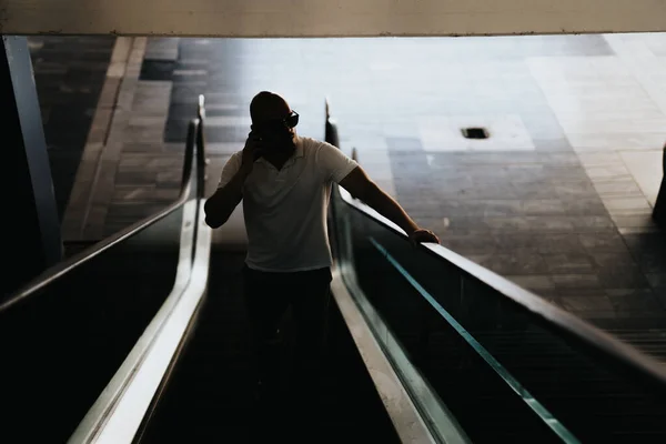 Businessman having phone call using escalator at big business center. Silhouette shot.