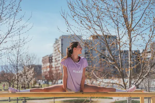 Health and physical activity concept. Happy sports girl doing splits exercises on horizontal bars in the park. Girl singing while stretching her legs in th park on horizontal bars