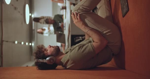 积极的男性员工一边休息一边用耳机听音乐和跳舞 坐在现代写字楼的凹陷处 — 图库视频影像
