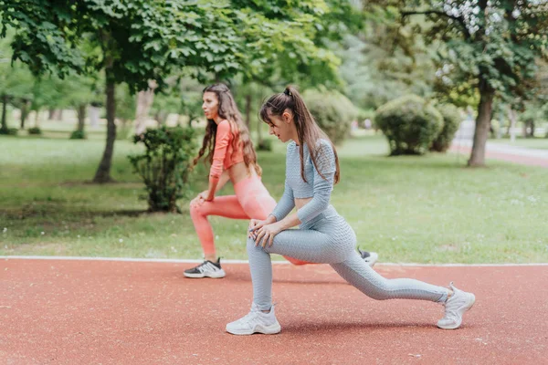 Two active women workout outdoors in an urban park, displaying their fit bodies and sport routine.