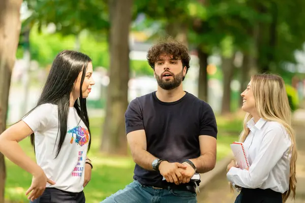 Male college student having a chat with his two female friends at the college campus outside on a sunny day