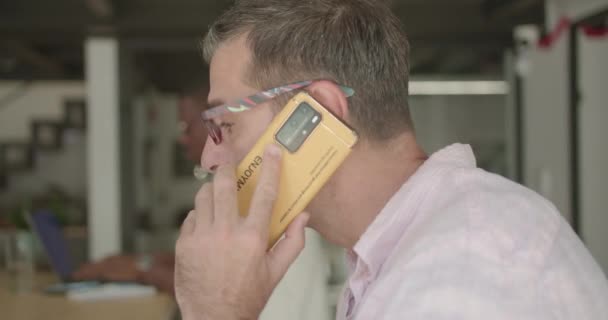 Egy Idősebb Férfi Beszél Telefonon Miközben Kollégái Hátul Dolgoznak — Stock videók