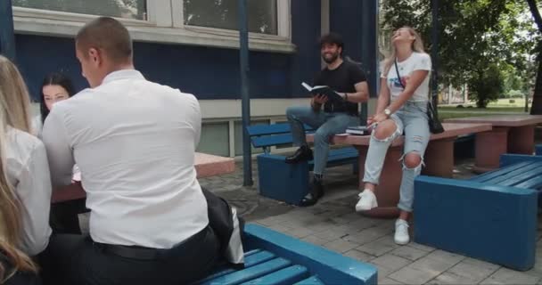 在大学校园外的一个城市里 一大群学生坐在长椅上 满满一长椅的书 用卡车运走知识 — 图库视频影像