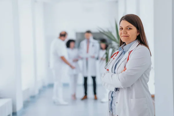 A confident female doctor in a medical clinic, wearing a white lab coat, poses with folded arms. With a satisfied smile, she exudes professionalism and success.