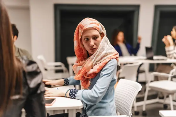 イスラム教徒の女性従業員は オフィスのテーブルでラップトップに取り組んでいる間に何かを見つめている — ストック写真