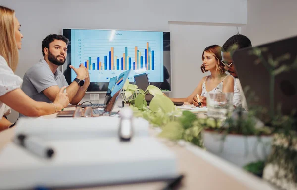 A diverse group of businesspeople in a modern conference room engage in a productive meeting, discussing goals, problem-solving, and profit growth.