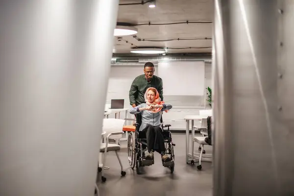 坐在轮椅上跳舞的快乐女人在办公室里被男同事推着 — 图库照片
