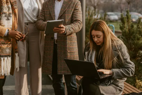 Close up of blonde business woman typing on the laptop while her colleagues working on the tablet while standing next to her