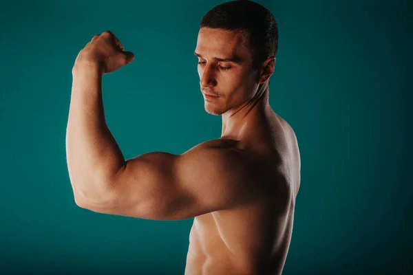 Aesthetic man standing in front of a green background and flexing his bicep