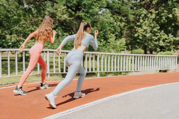 Two active and attractive women do a sport routine in an urban park. They stretch, work out, and inspire each other.