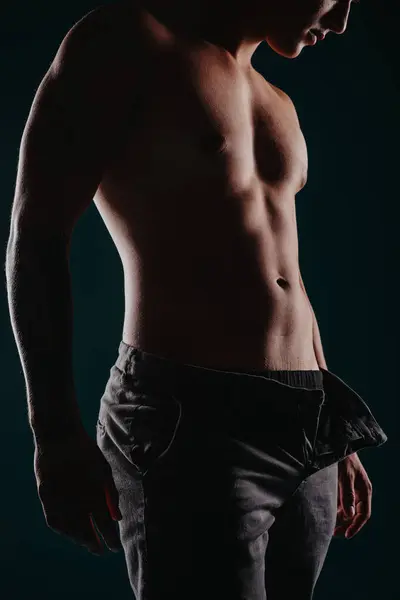 フィットする男性アスリートは 彼の強くて筋肉的なビルドを示しています 彼はモチベーションを持ってポーズし 彼の変身した体と明確に定義された筋肉を黒い背景に表示します — ストック写真