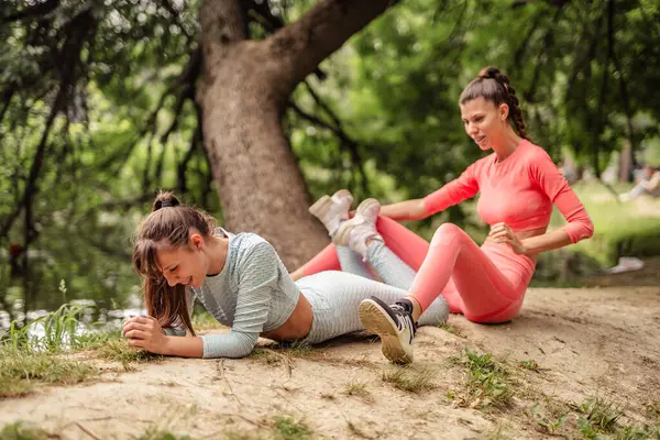Active, fit females doing stretching exercises in a city park. Friends training outdoors, exhibiting energy and stamina. Vibrant urban sport routine among trees.