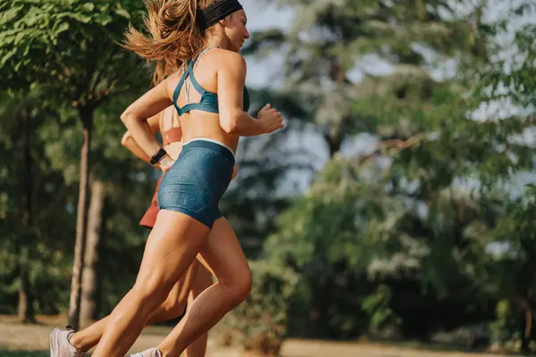 Athletic women jogging outdoors in green surroundings, showcasing their fit bodies and inspiring fitness.