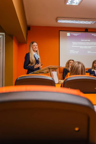 Young university student giving a speech on the podium defending her diploma at the conference room in front of the professors and students