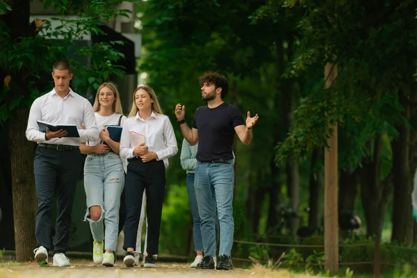 4人の大学生が手で学び 外で勉強する本と一緒に歩いています — ストック写真