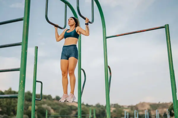 フィットガールは屋外で温め ストレッチし 金属棒に柔軟にします 運動体は健康でアクティブなライフスタイルを刺激します トレーニング前に強さと柔軟性を示すスポーティな女性 — ストック写真
