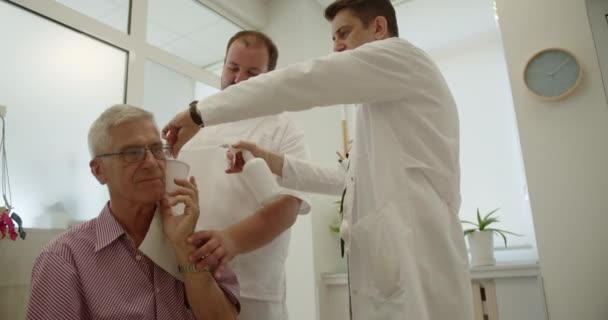 Doświadczeni Męscy Lekarze Rozmawiający Podczas Czyszczenia Uszu Starszego Pacjenta Pokoju — Wideo stockowe