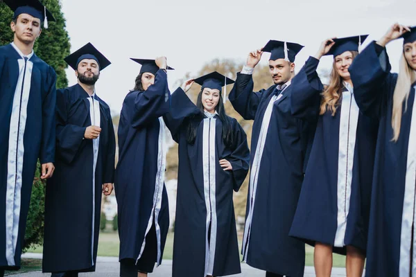 即将毕业的大学生们一起在公园里 穿着礼服和帽子 一边笑一边扔帽子 庆祝自己的成就 永远的美好回忆 — 图库照片