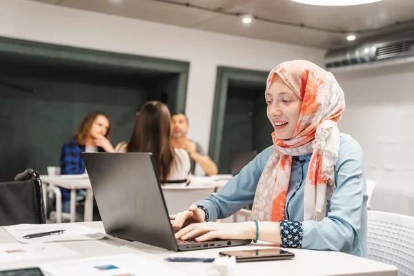 有重点的女员工头戴头巾 在膝上型电脑上工作 面带微笑 — 图库照片