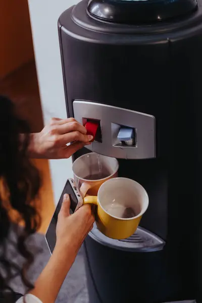 Woman Employee Pouring Hot Water From The Dispenser While Taking a Break to Enjoying Her Fresh Tea