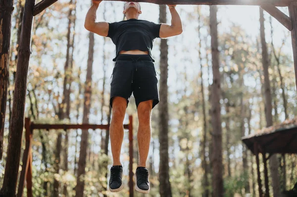 Active man enjoying sunny day doing pull ups outdoors. Fresh air and forest landscape perfect for physical activity, healthy lifestyle, hiking, and camping.