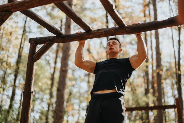 Healthy sportsperson doing pull ups amidst trees and mountains, enjoying outdoor adventure. Hiking, exercising cardio, and exploring green natural environment on weekend getaway.