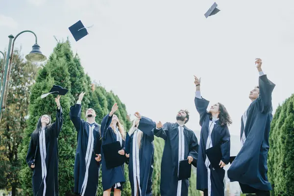 成功地从大学毕业后 身穿长袍的学生们把帽子抛向空中 给人留下了美好的回忆 — 图库照片