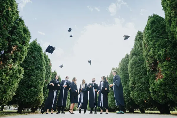穿着毕业礼服的快乐学生们 在庆祝他们的成就和毕业时抛出了帽子 — 图库照片