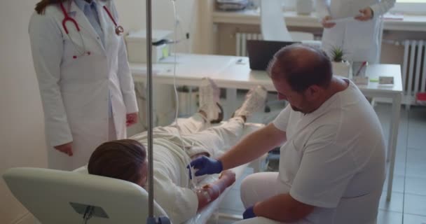 三名医生 包括男医生和女医生 在阳光照射的医疗实验室给一名年轻病人输液 — 图库视频影像