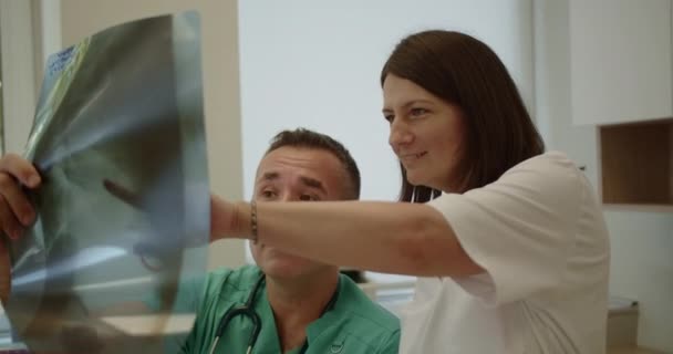Опытный Специалист Обсуждает Рентгеновские Снимки Своей Медсестрой Средних Лет Офисе — стоковое видео