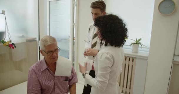 Μεσήλικας Άντρας Γιατρός Και Υπέροχη Νοσοκόμα Του Πλένουν Αυτιά Ηλικιωμένων — Αρχείο Βίντεο